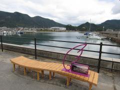 海の見える場所に置かれている波のような曲線のある、間伐材で作られたアートベンチの写真
