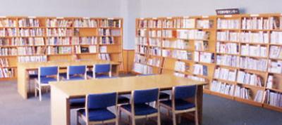 テーブルが2つあり、壁際の本棚に本が並んでいる写真