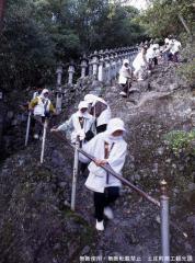 白い寺用作務衣を着た女性たちが手すりを使いながら岩道を下りている写真